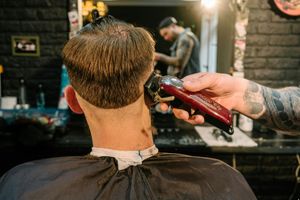 A barber using clippers to trim the back of a client's hair in a salon.
