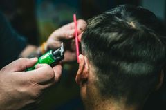 A barber uses electric clippers and a bright pink comb to trim hair around a client's ear.