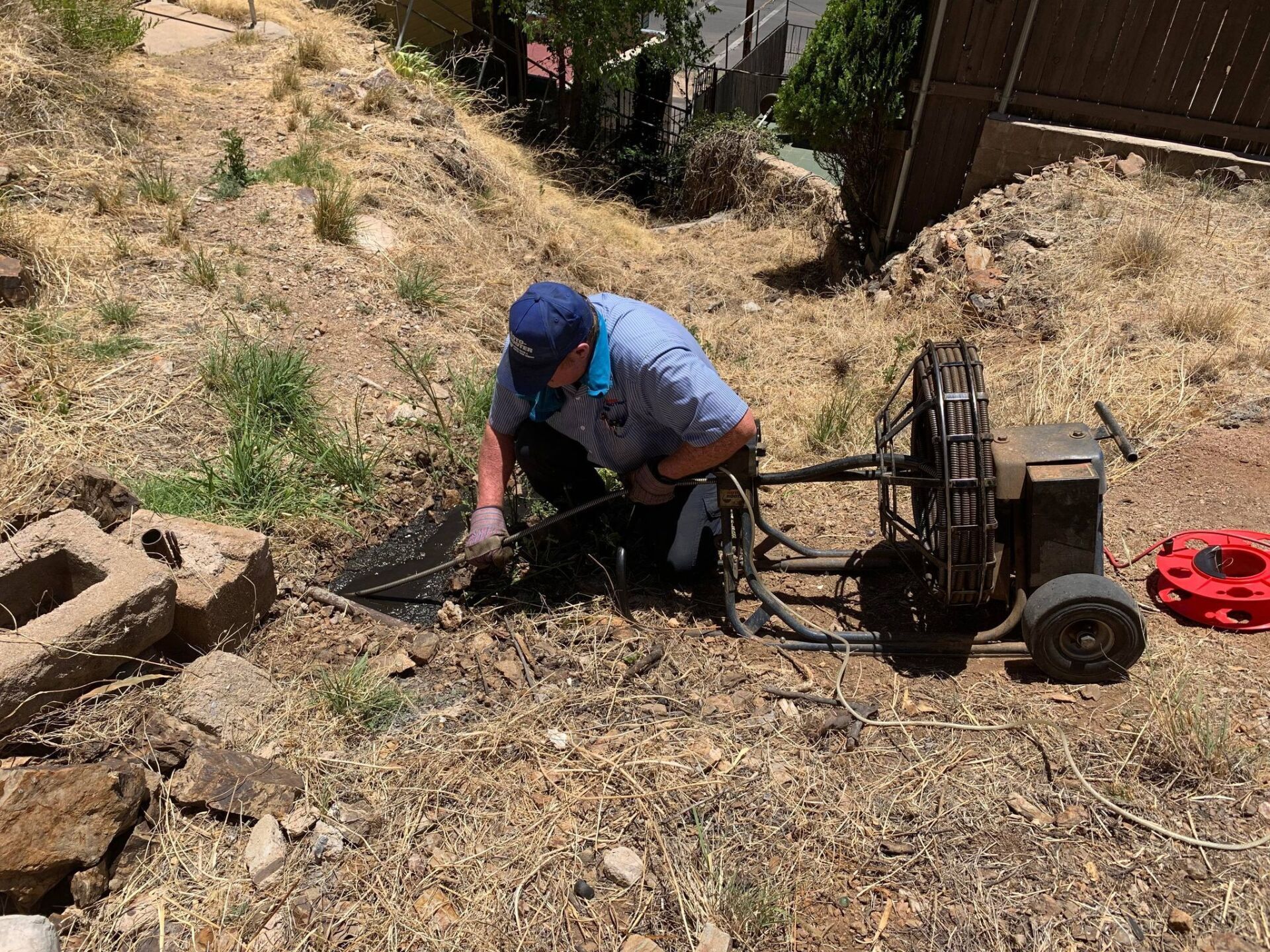 A man is kneeling down in the dirt next to a machine.
