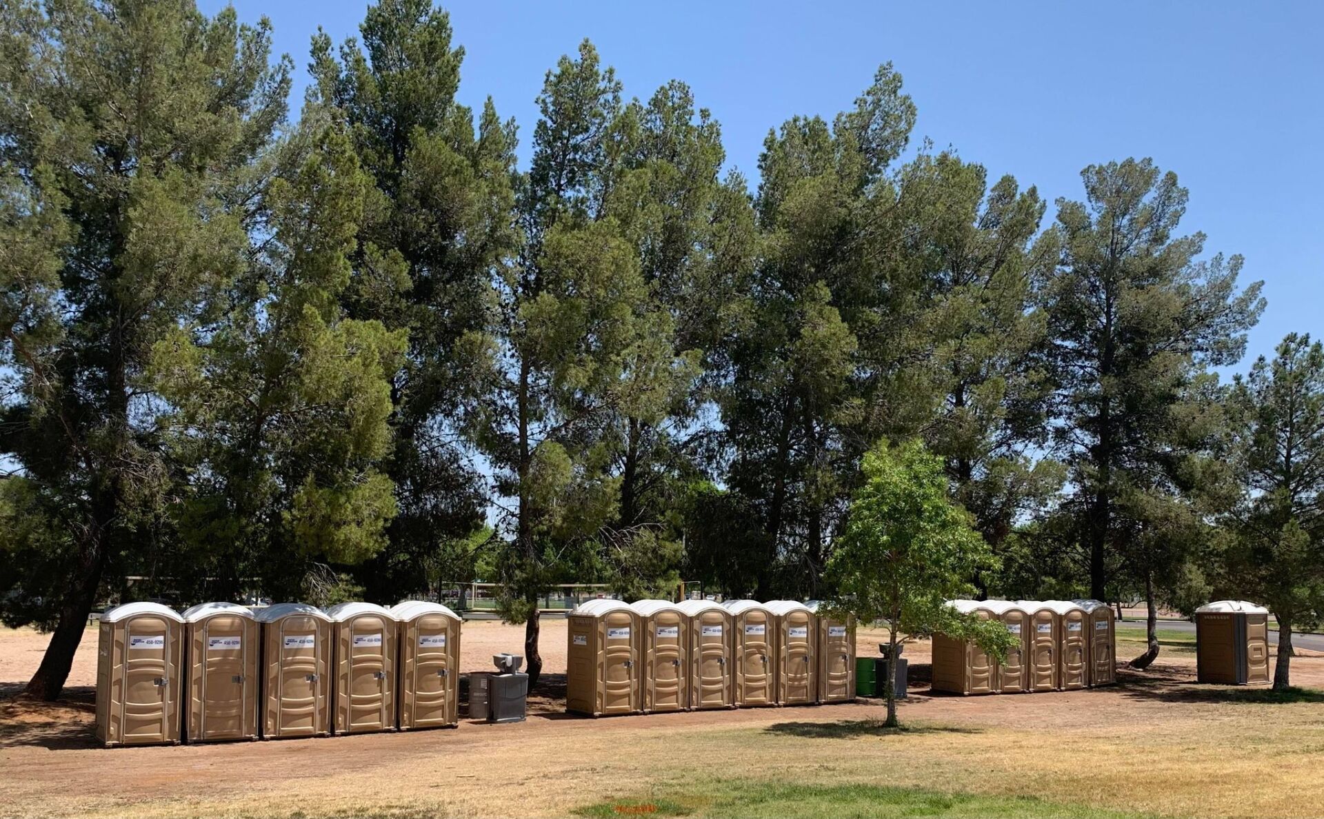 A row of portable toilets in a park with trees in the background