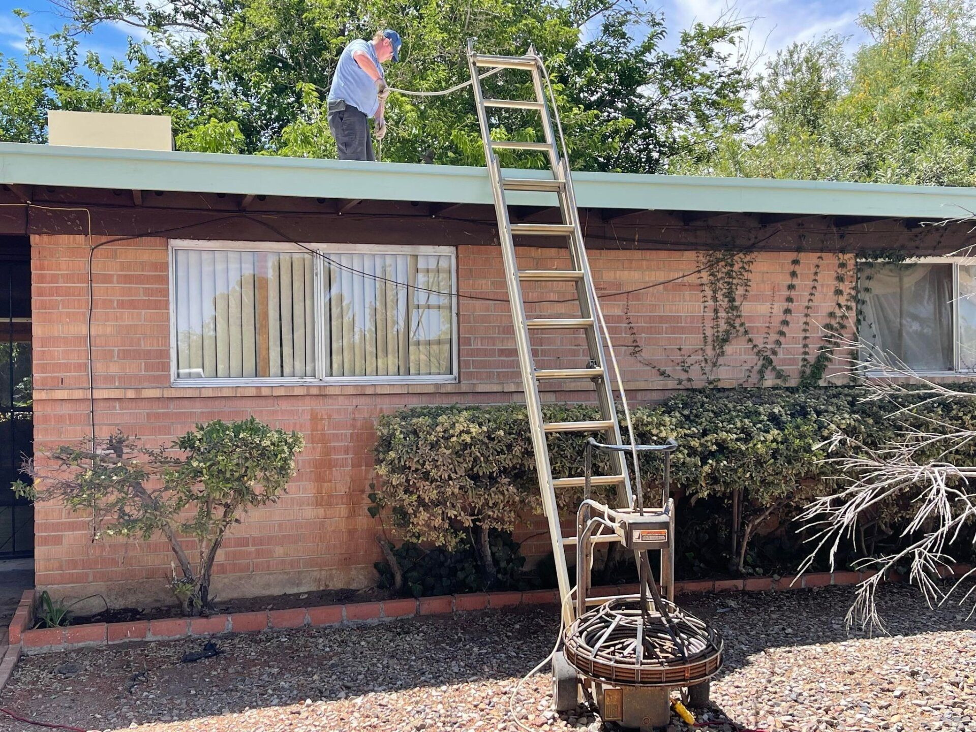 A man is standing on the roof of a house with a ladder attached to it.
