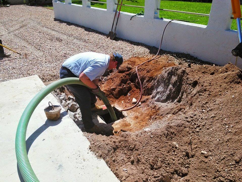 A man is using a green hose to dig a hole in the ground