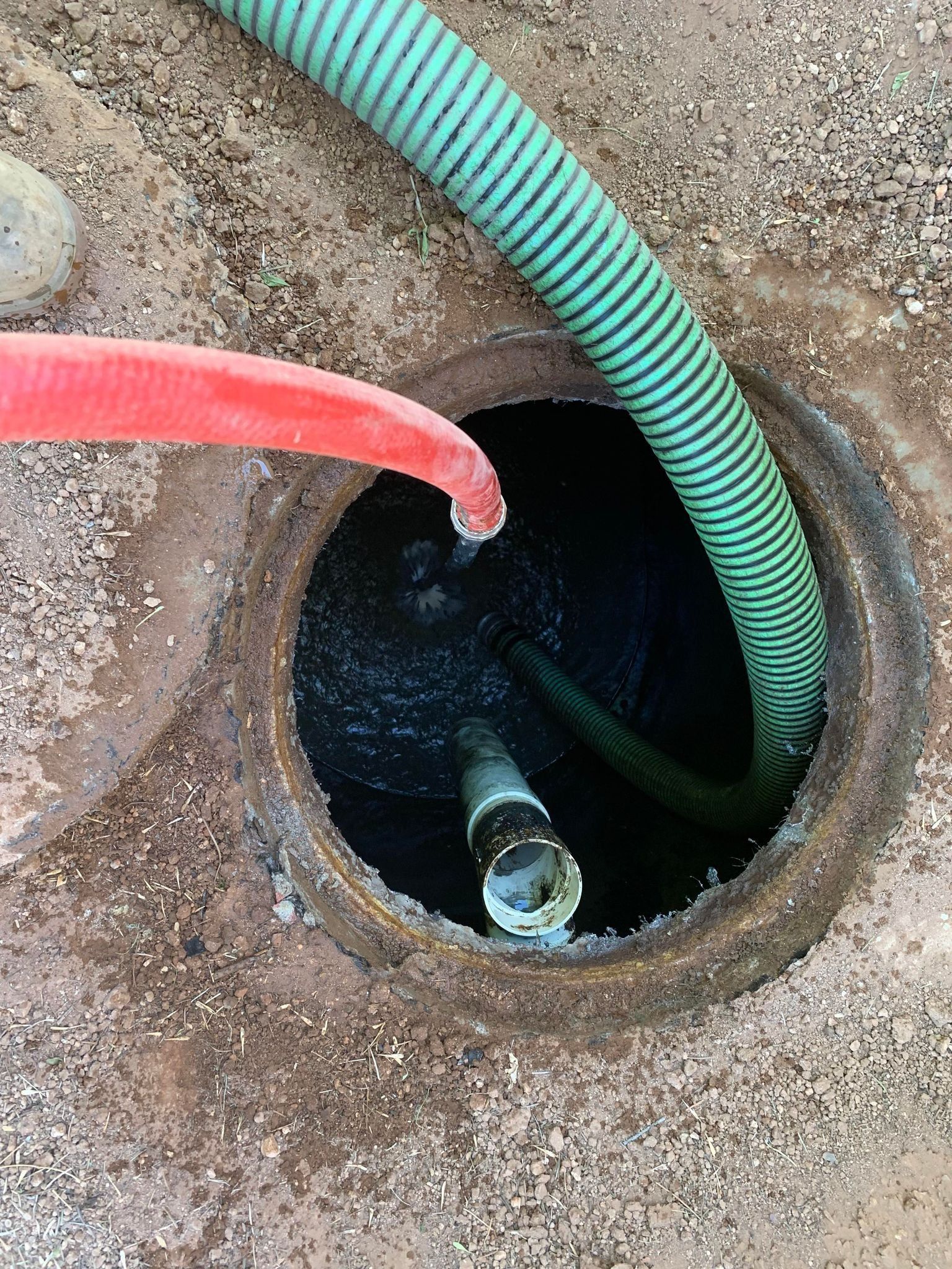 A green hose is being used to pump water into a manhole.