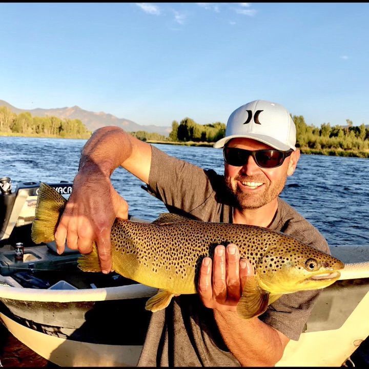 A man in a hurley hat is holding a brown trout