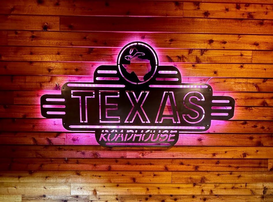 A neon sign for texas roadhouse is lit up on a wooden wall.