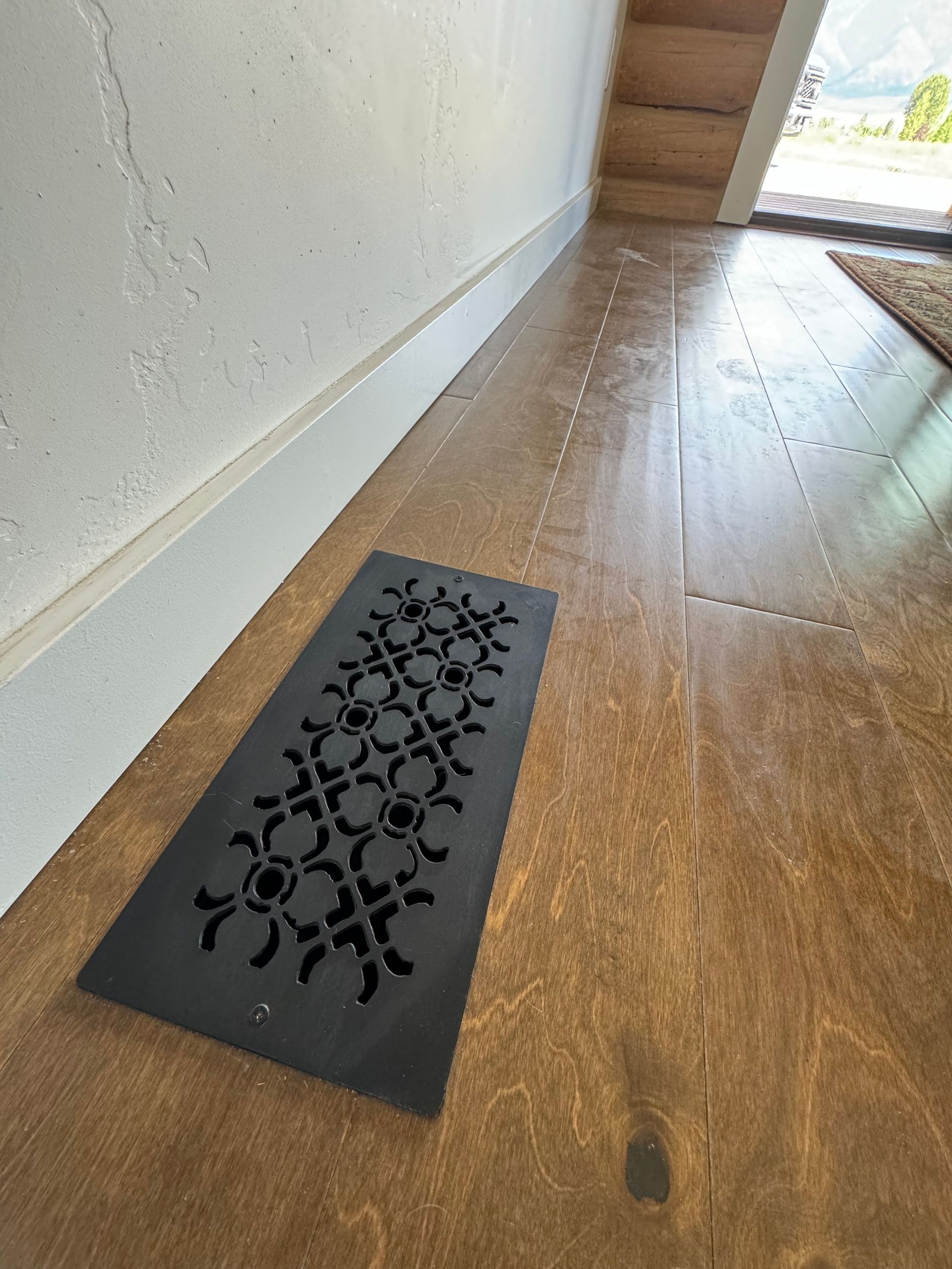 A black mat is sitting on a wooden floor next to a wall.