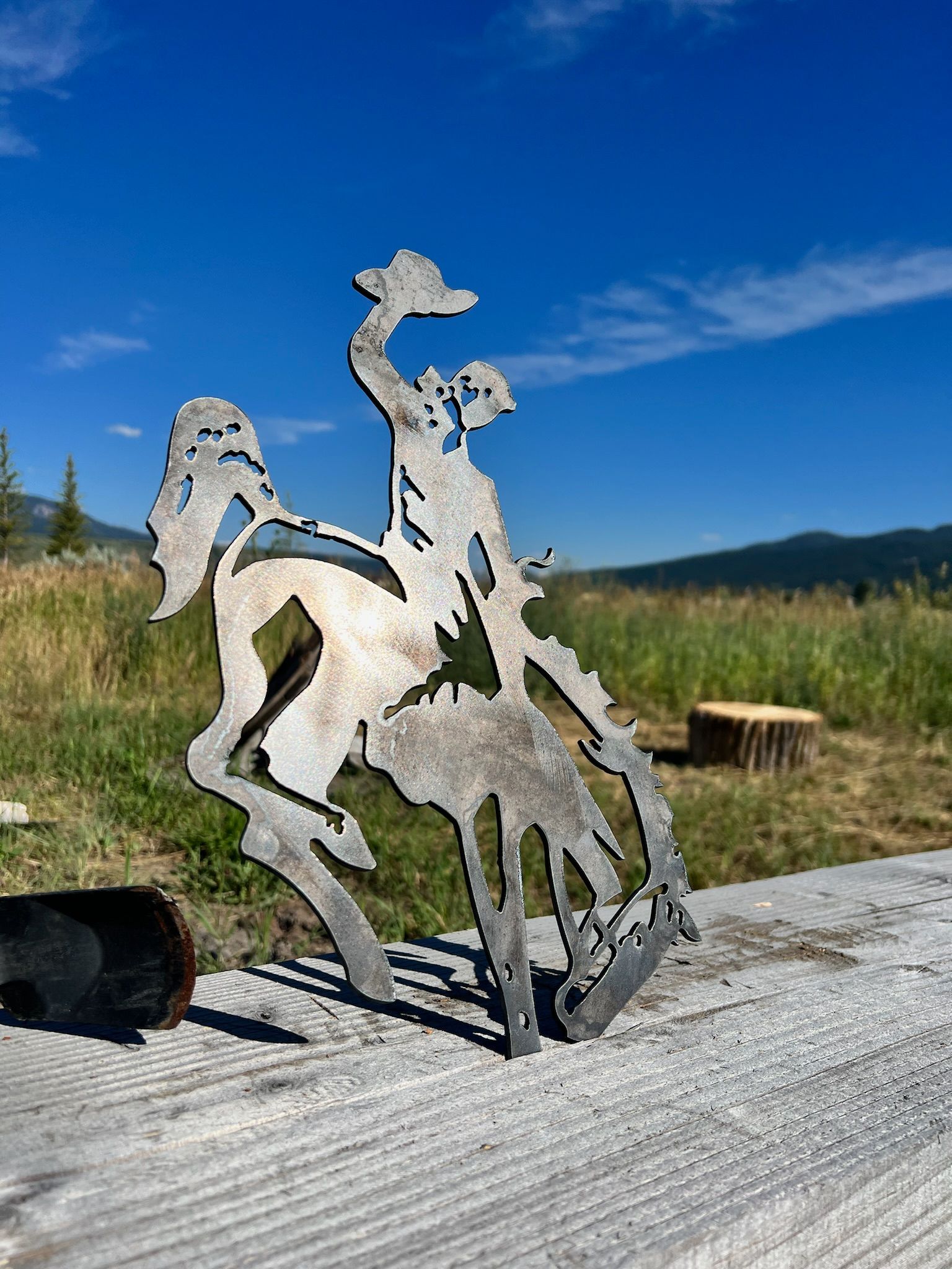 A metal sculpture of a cowboy riding a horse is sitting on a wooden table.