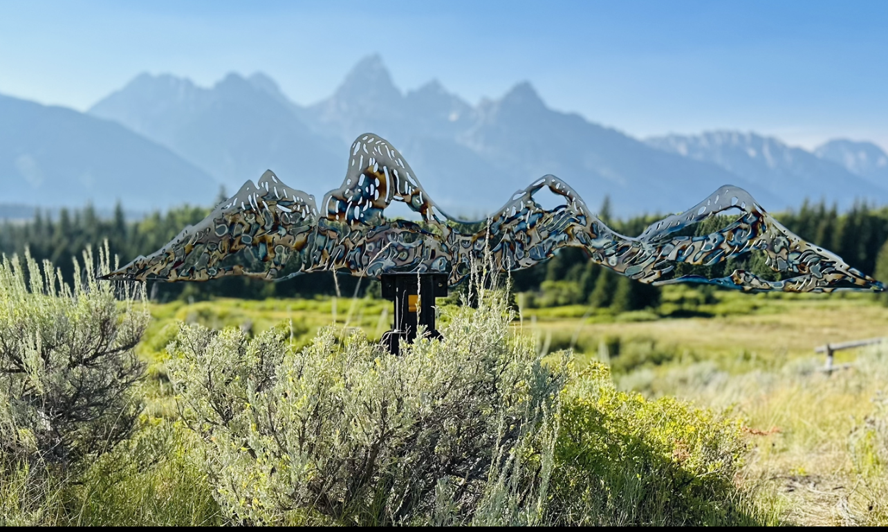 A sculpture of a mountain range in a field with mountains in the background.