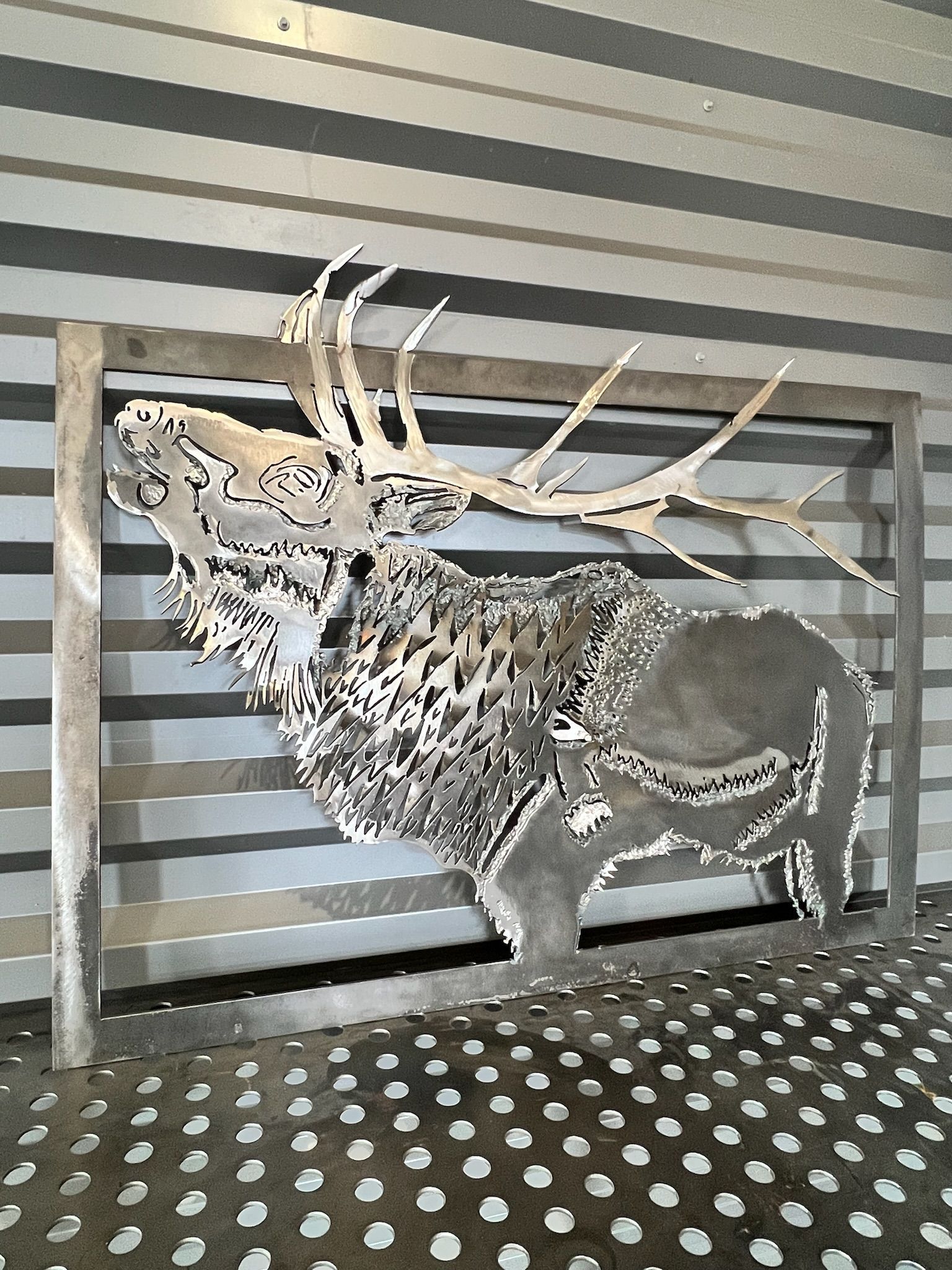 A statue of a deer with antlers is standing in front of a striped wall.