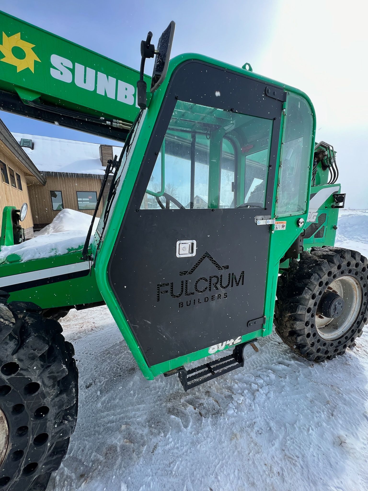 A green tractor is parked in the snow in front of a building.