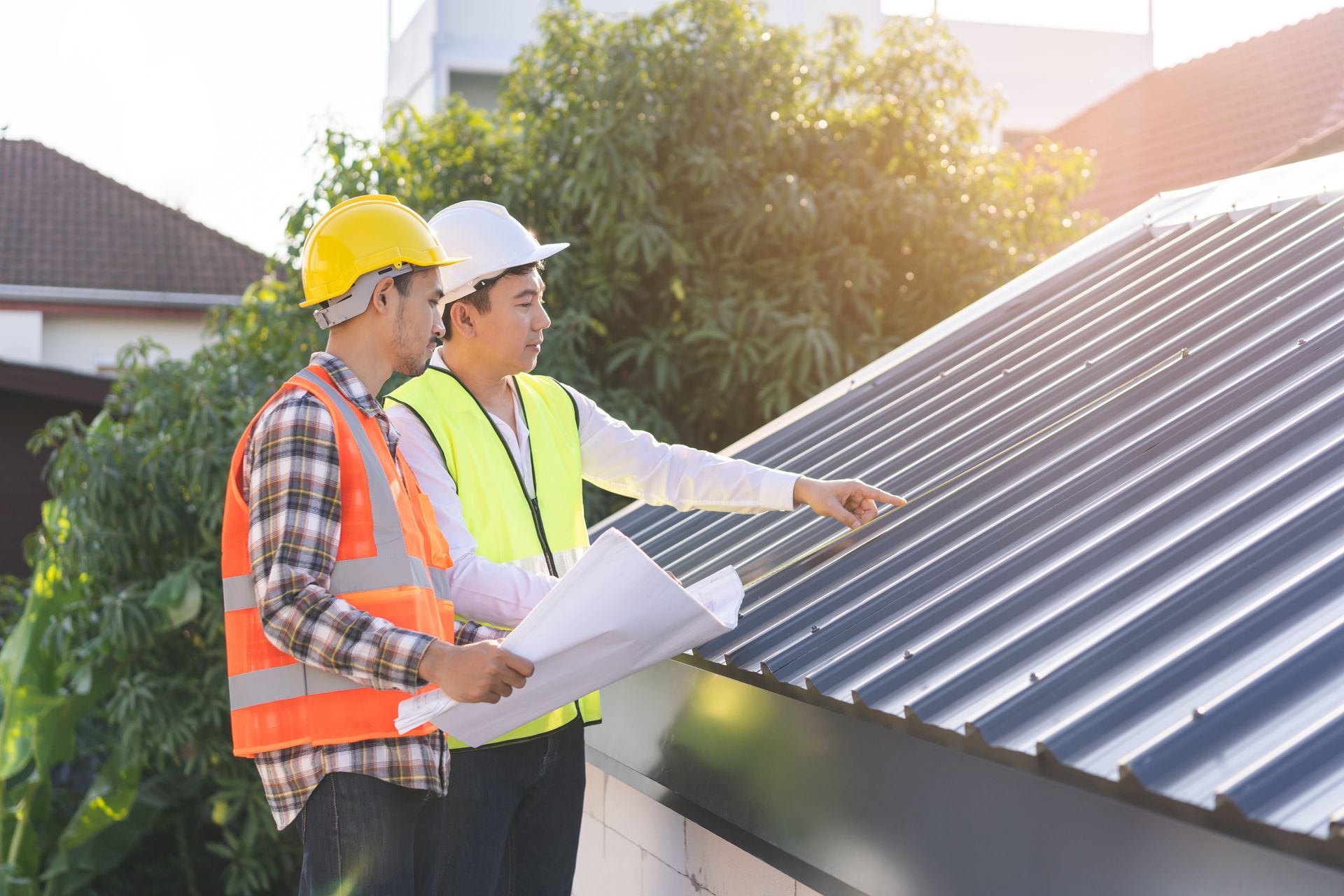 A foreman and contractor in helmets are discussing a metal sheet rooftop on a blueprint.