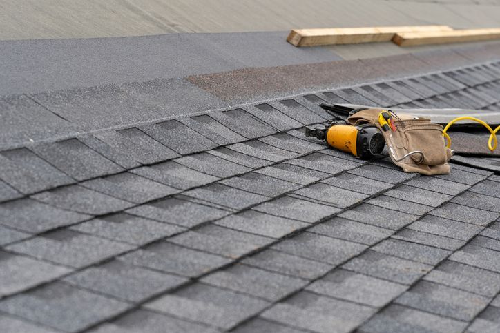 Rooftop with gray shingles, nail gun, and tools. Construction in progress.