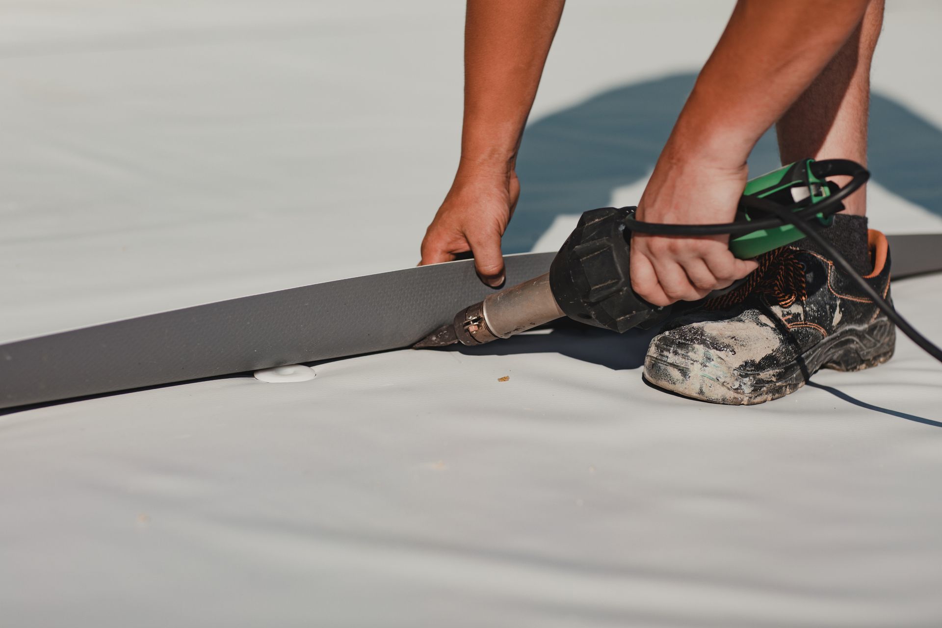 Person using a heat gun to seal a gray strip onto white roofing material.