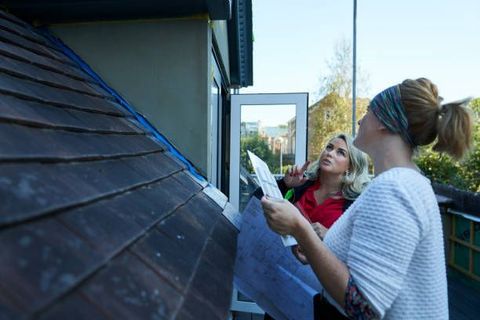 Two women, one in red shirt, the other in white, looking at documents outside a building.