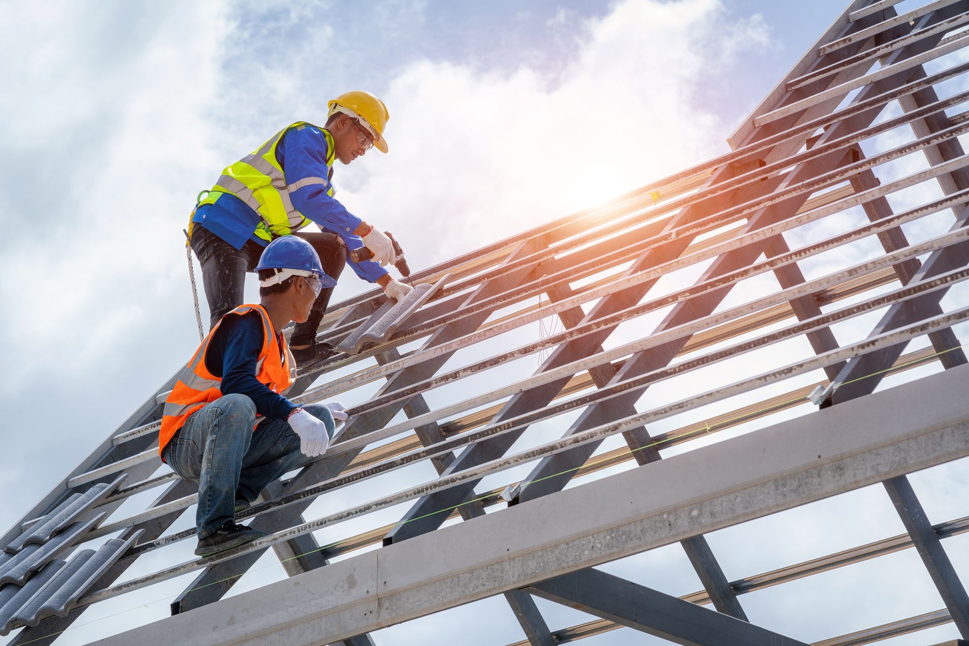 Two construction workers installing metal roofing on a frame, wearing helmets and safety vests, with a bright sky.