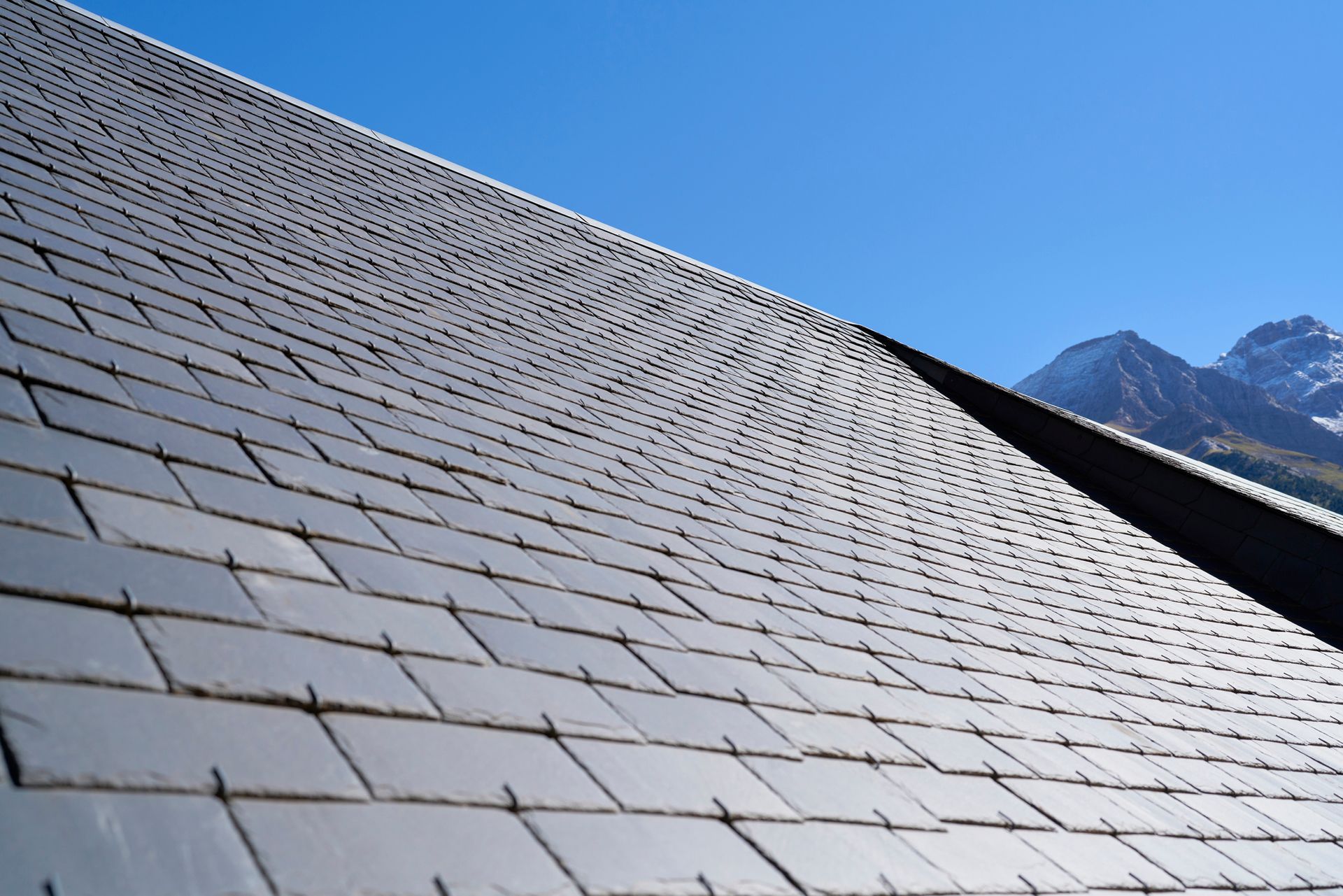 Slate roof against a bright blue sky, with mountain peaks visible in the background.