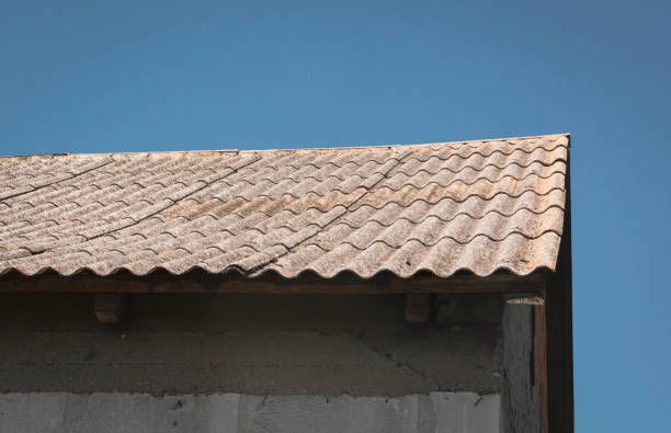 Corner of a building with gray, wavy roof tiles against a bright blue sky.