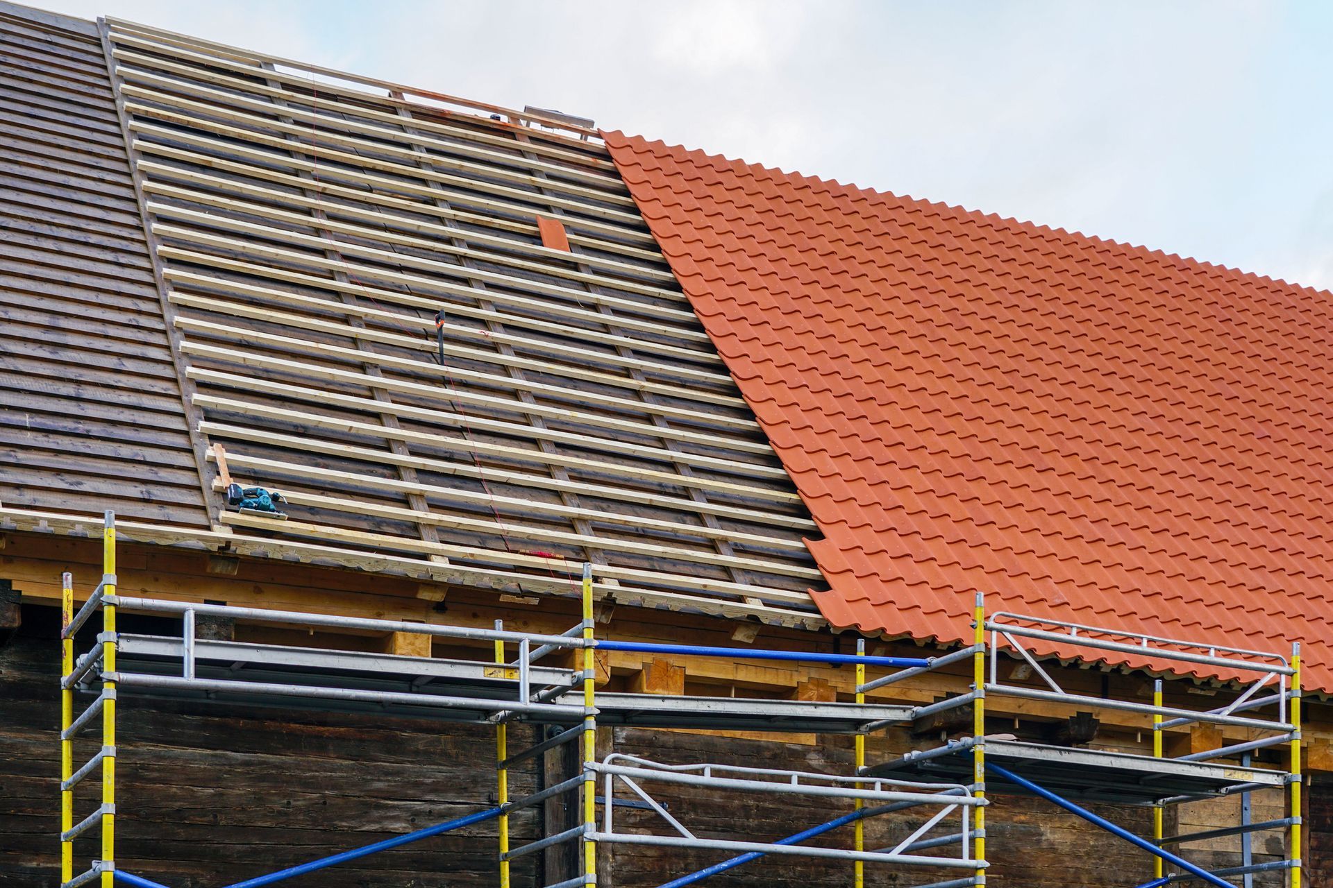 Roof replacement in progress: orange and brown tiles, scaffolding, sky backdrop.