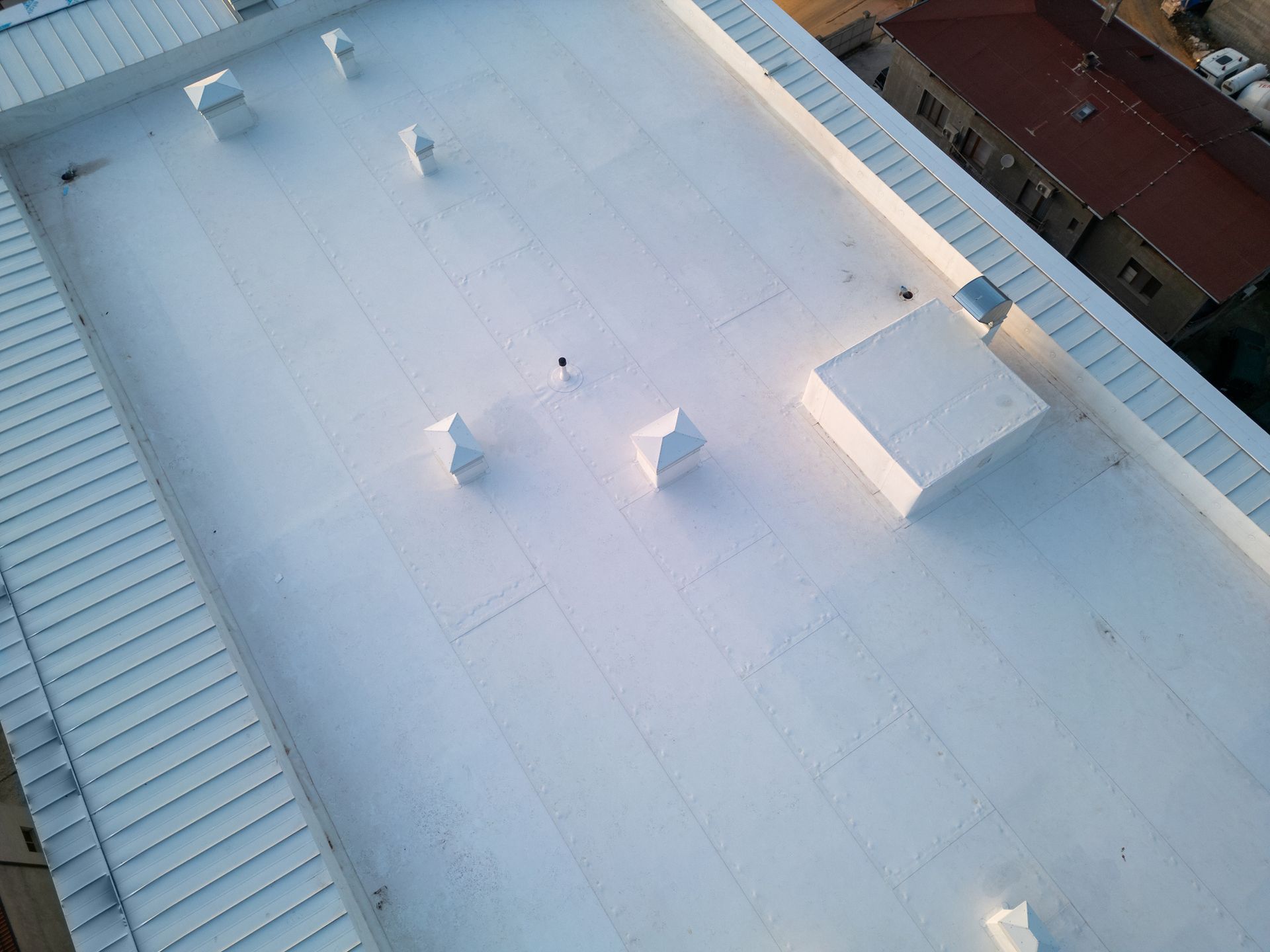 White flat commercial roof with vents, near buildings.