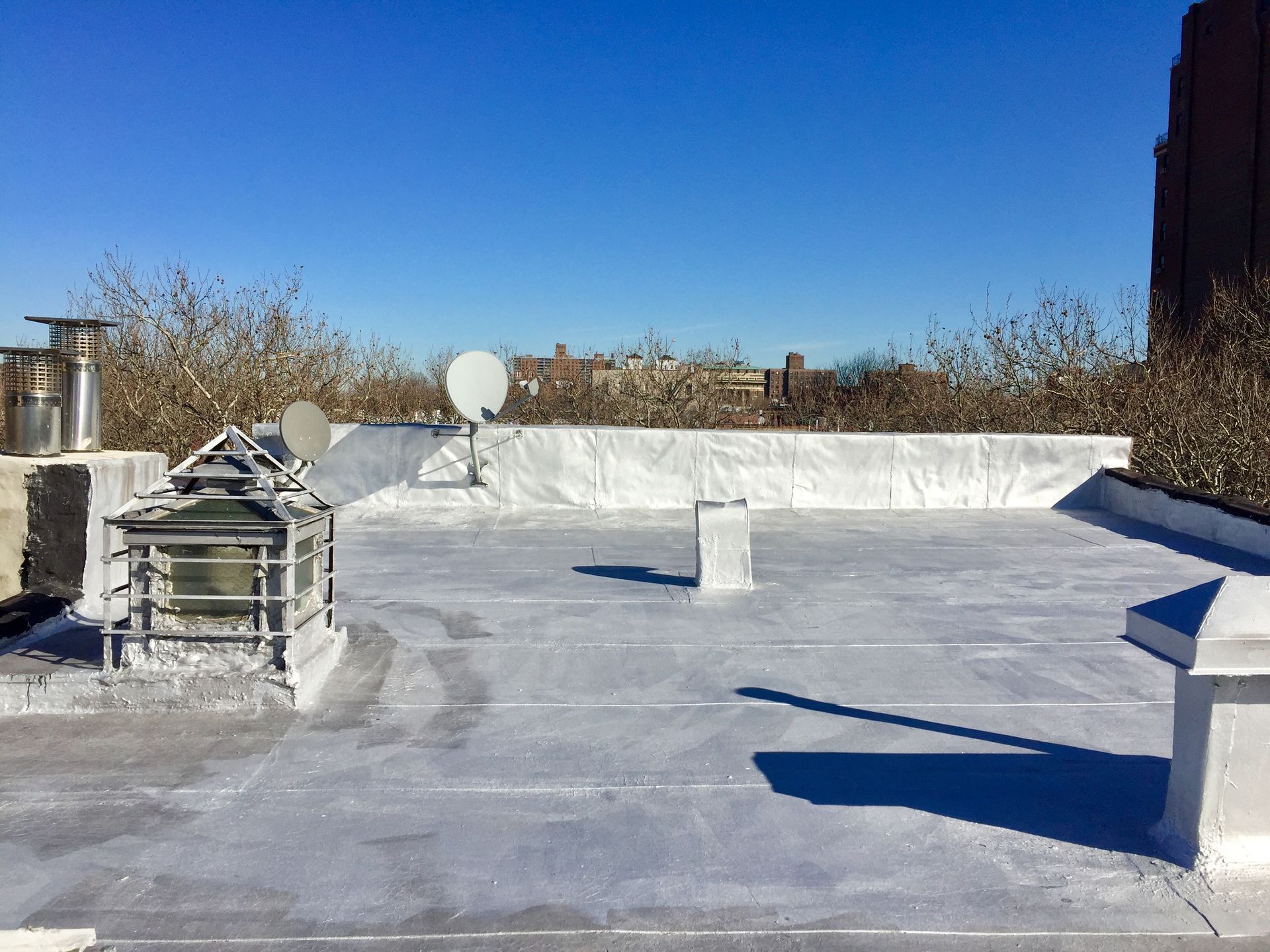 Rooftop view of a building with a white coating, various structures, and a clear blue sky in the background.