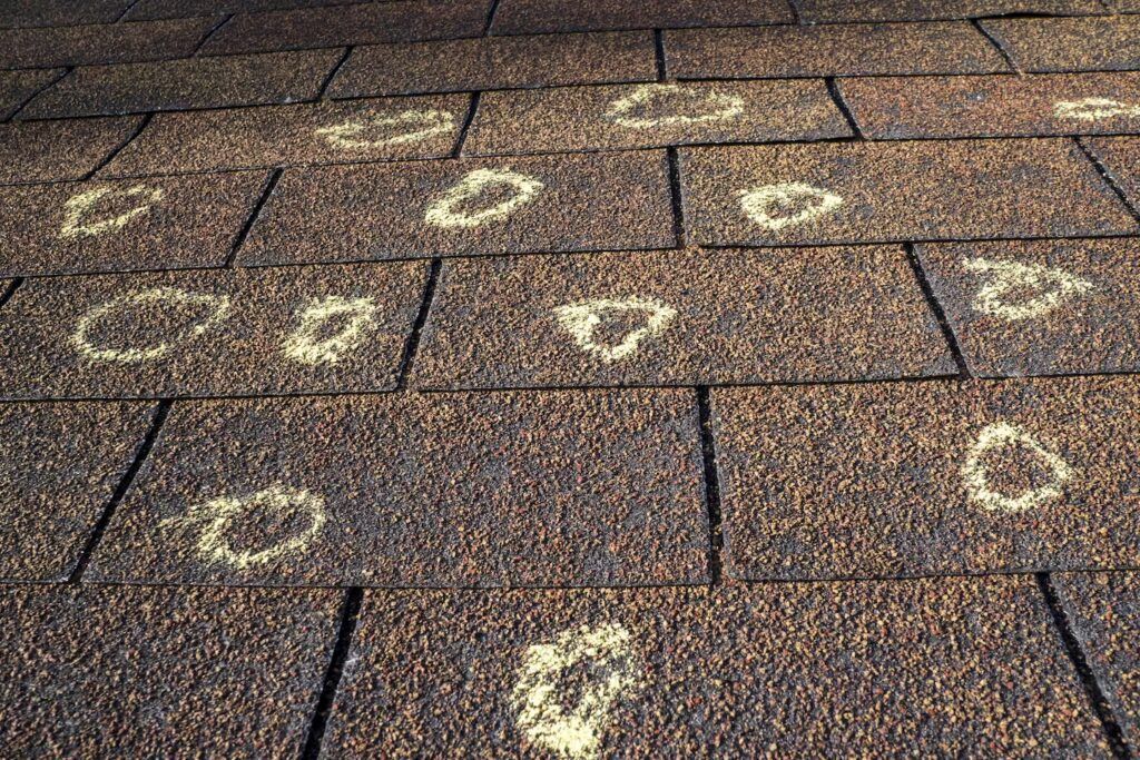 Hail-damaged brown asphalt roof shingles marked with yellow chalk circles.