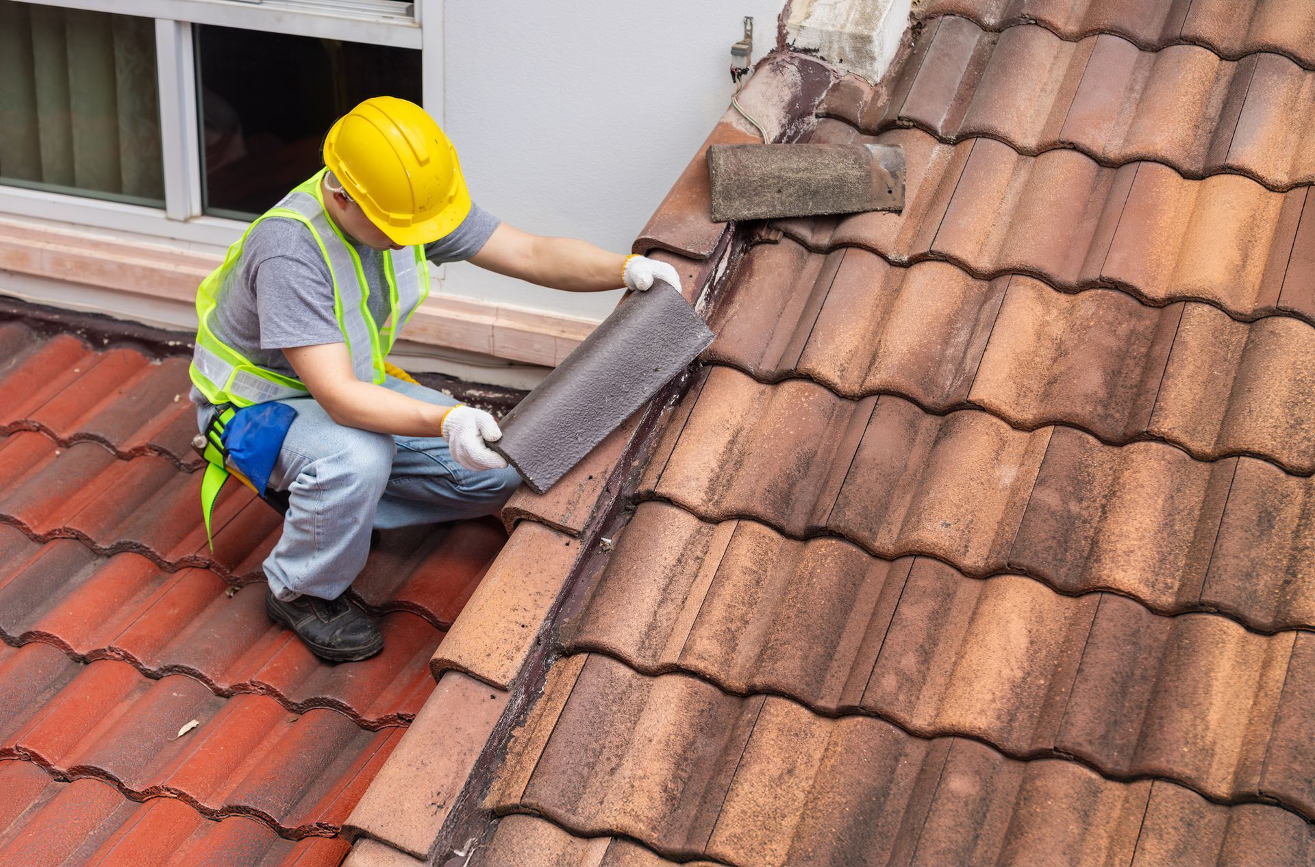 Roofer in hard hat and safety vest installing a tile on a terracotta tile roof.