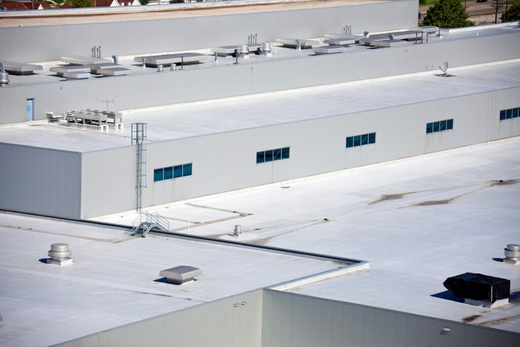 Workers on a rooftop removing shingles. Gray roof, sunlight, and safety ropes visible.