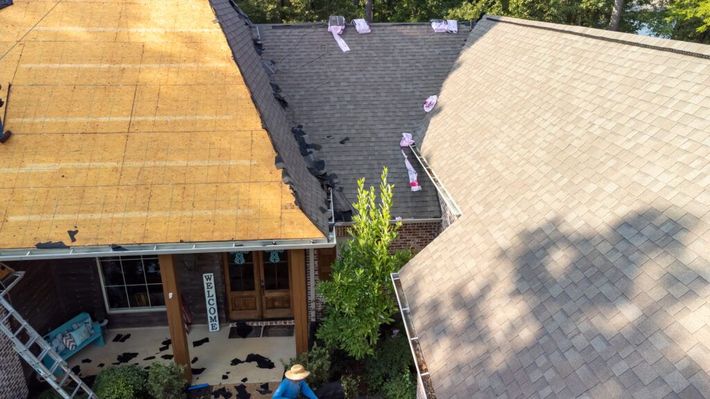 Overhead view of a house with a roof partially under construction; workers, trees, and ladder visible.
