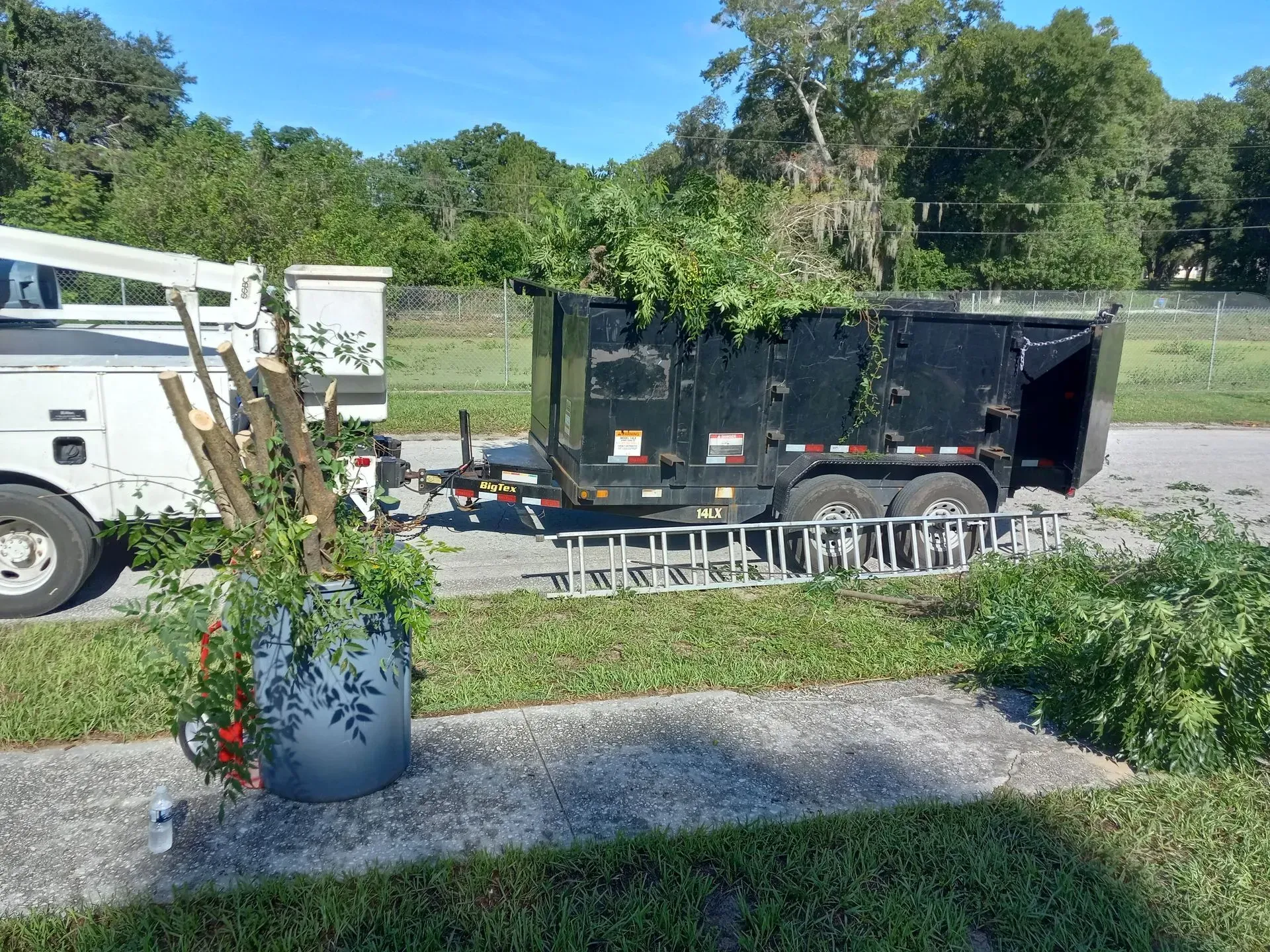 White utility truck hauling a black trailer beside stacked metal racks on a roadside in a green field
