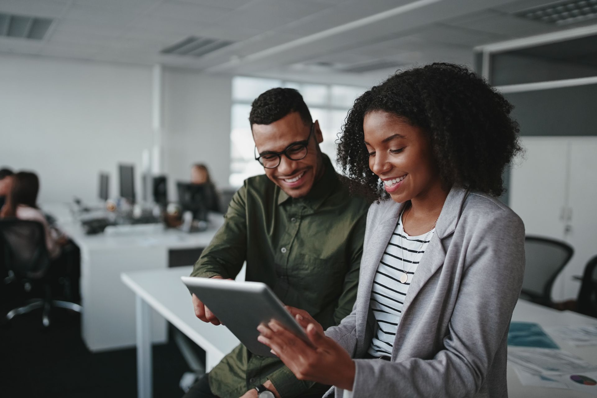 Two coworkers smiling and reviewing a tablet in a modern office