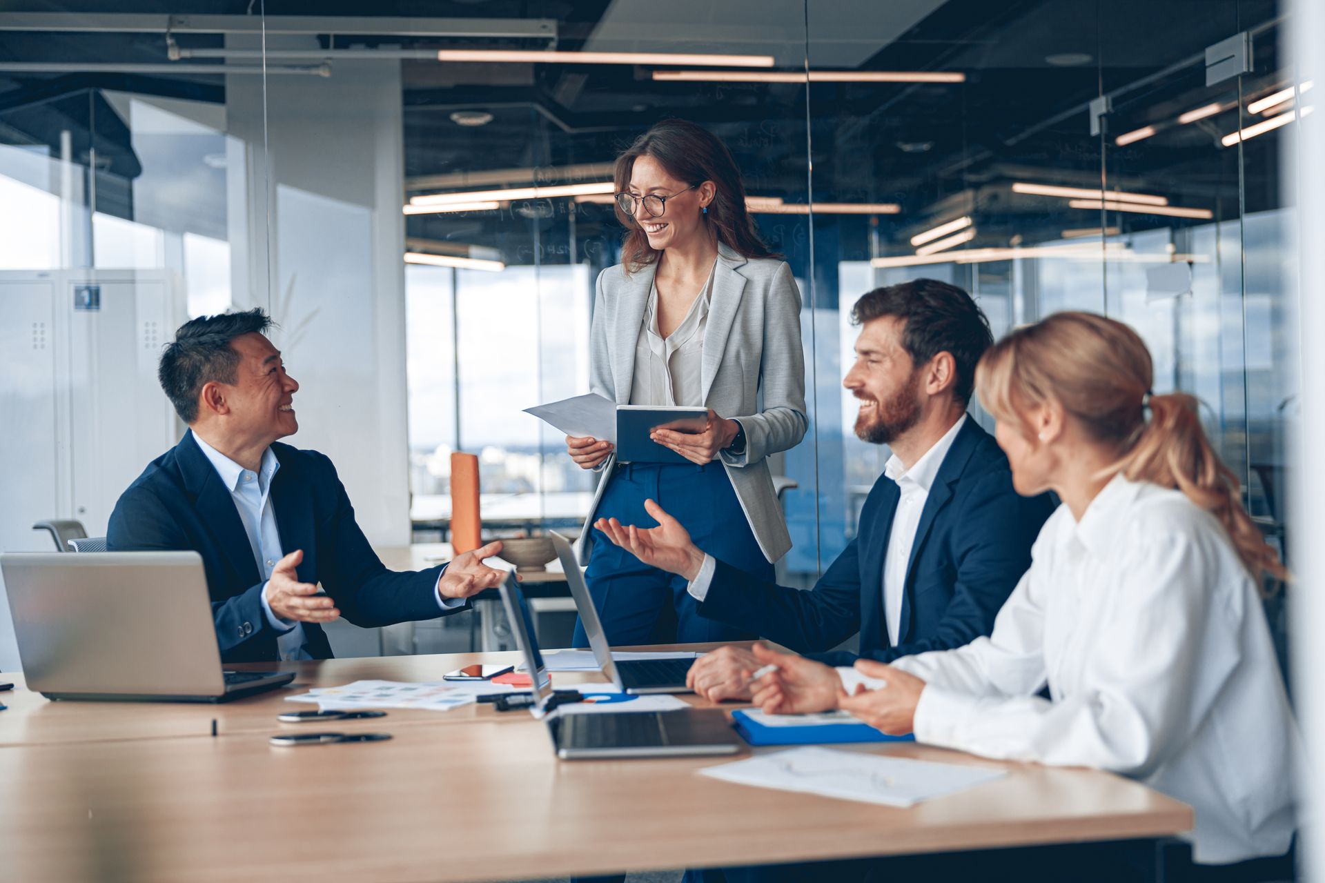Business meeting in a modern office, with colleagues discussing around a table and one woman presenting documents.