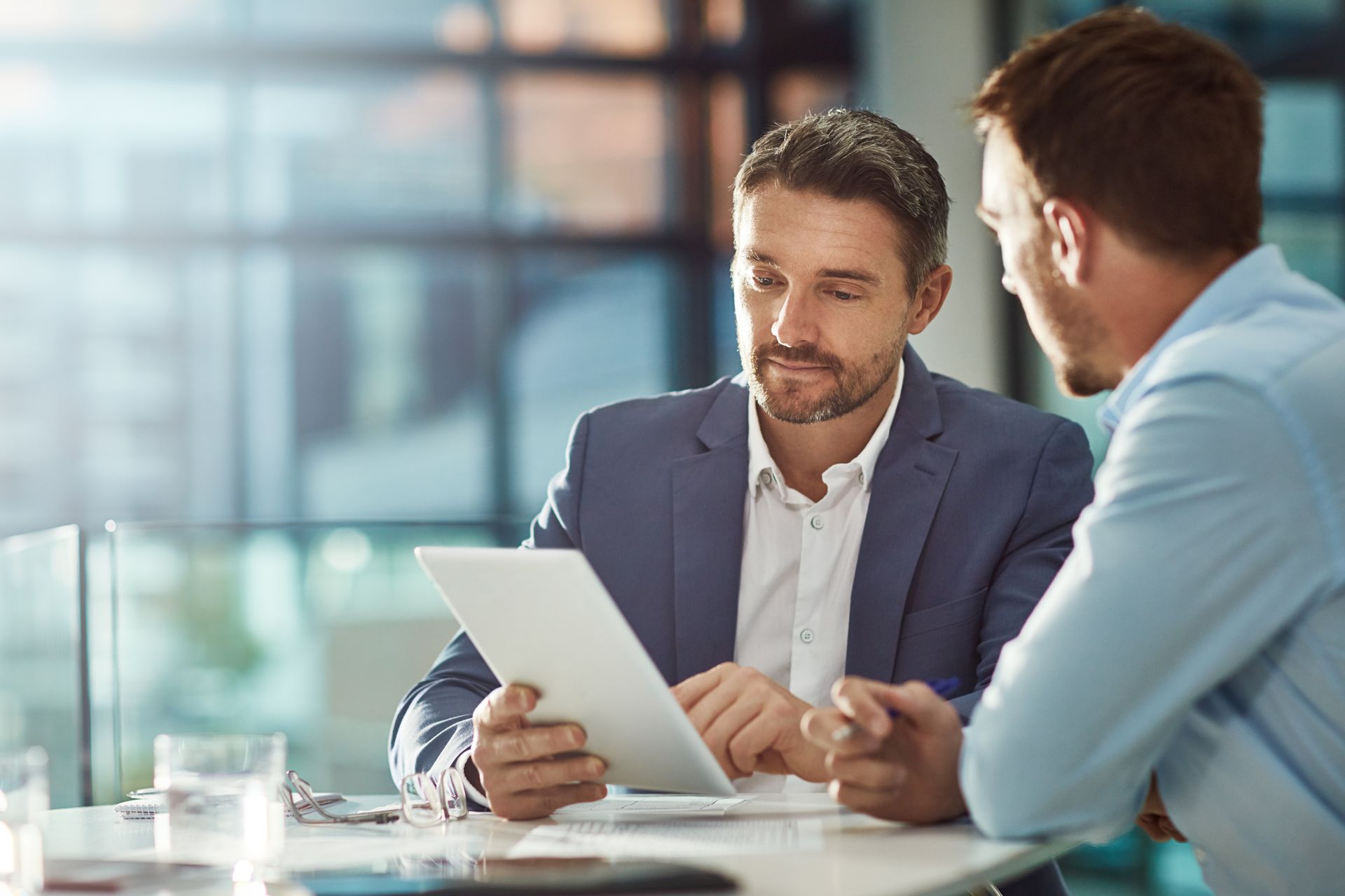 Two coworkers in a bright office reviewing a tablet together at a table