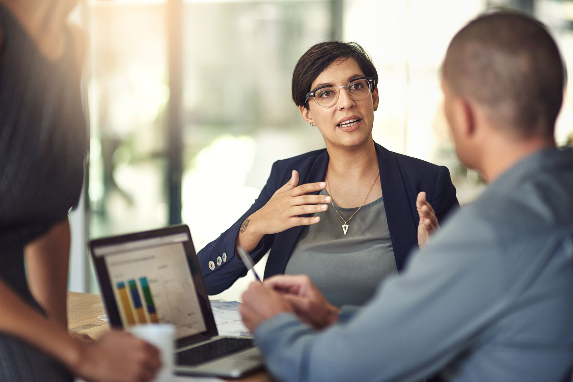 Business meeting with a presenter speaking to two colleagues beside a laptop and chart