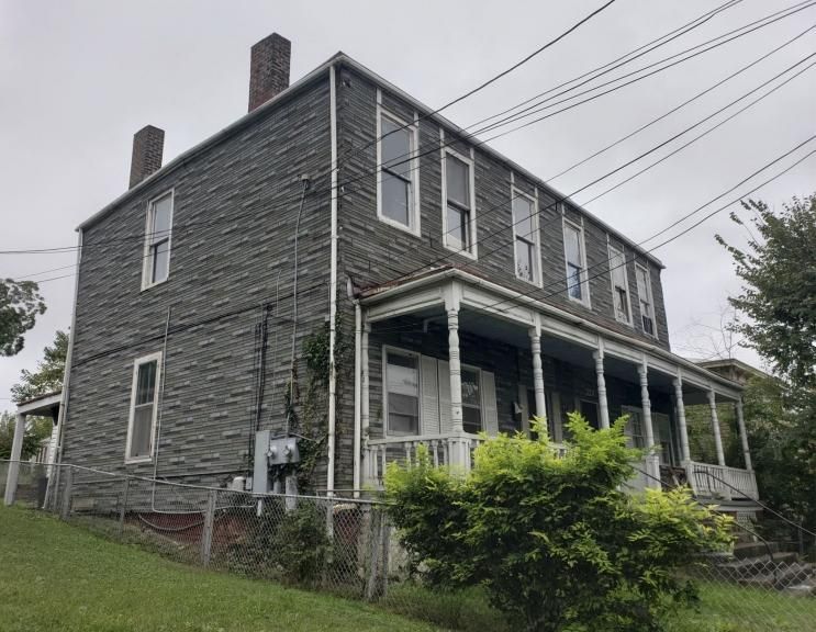 A large brick house with a porch is sitting on top of a grassy hill.