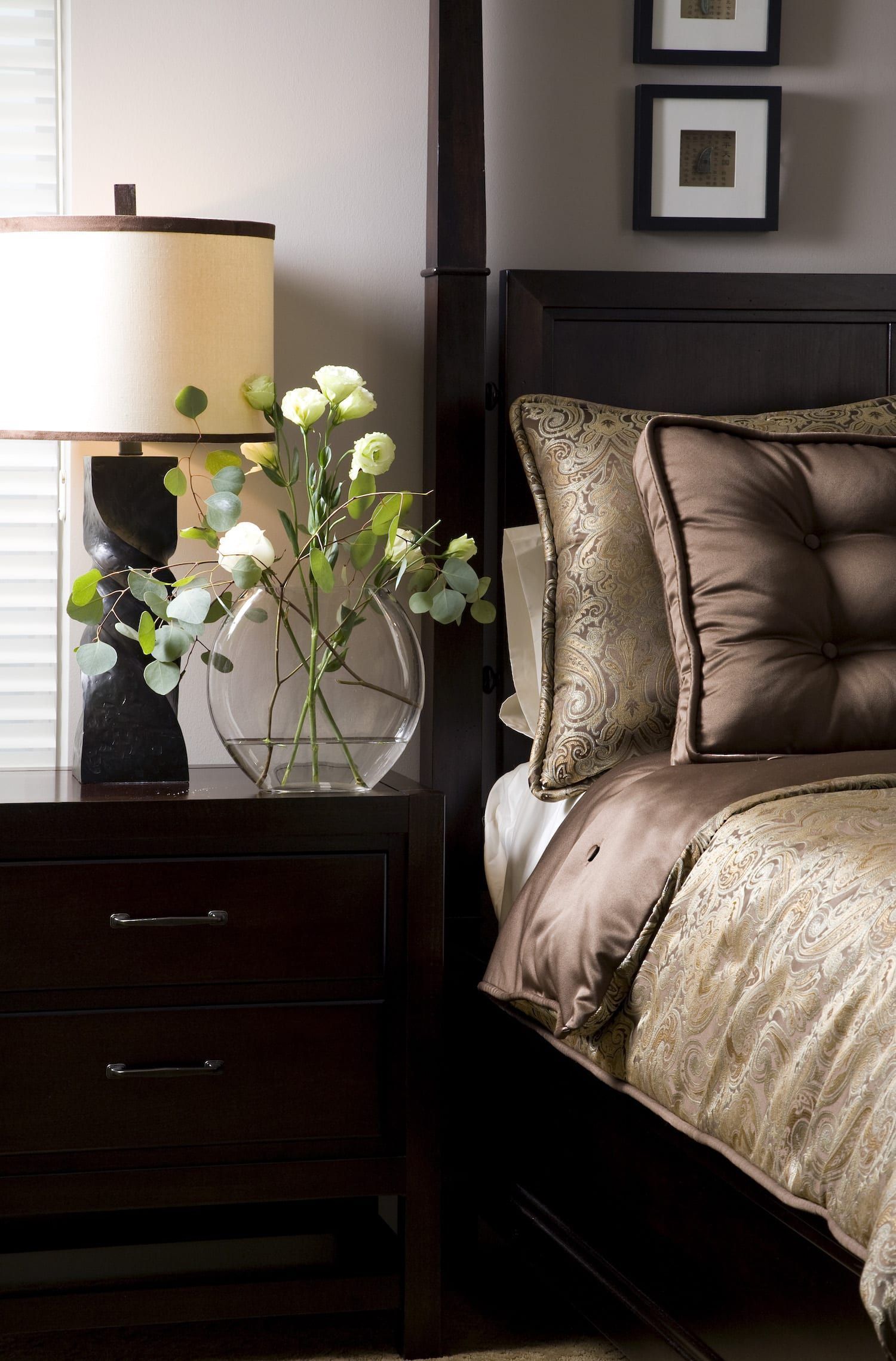 A vase of flowers sits on a nightstand next to a bed.