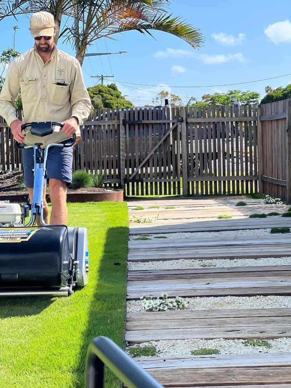 A Man Is Mowing A Lush Green Lawn With A Lawn Mower — The Garden Folk In Ballina, NSW