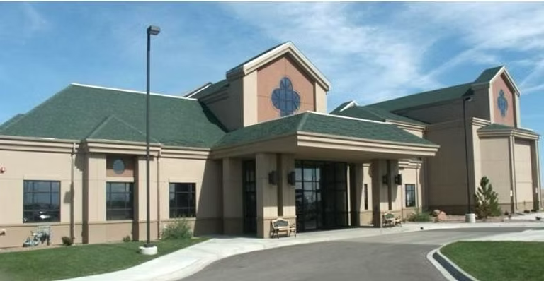 Tan building with green roof, arched windows, and a covered entrance.