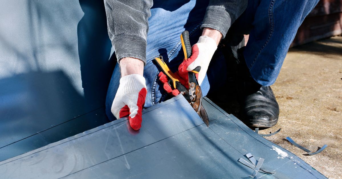 A worker at a construction site wearing gloves and using a pair of sheers to cut a piece of metal.