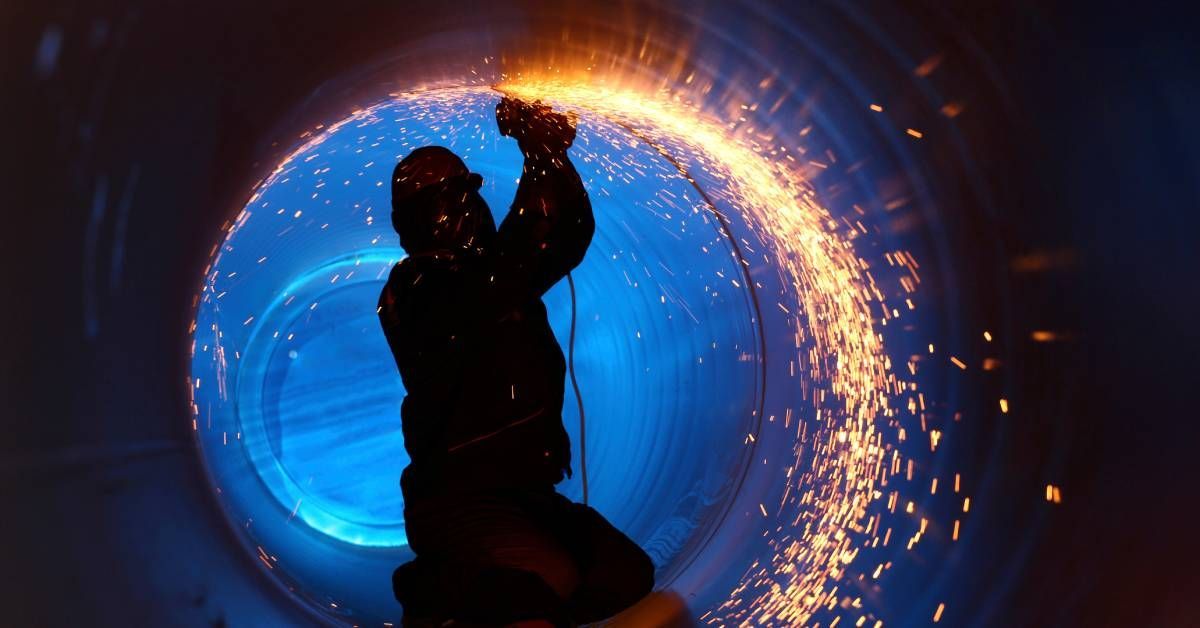 The silhouette of a worker inside a large industrial pipe. The worker is using a welder and there ar