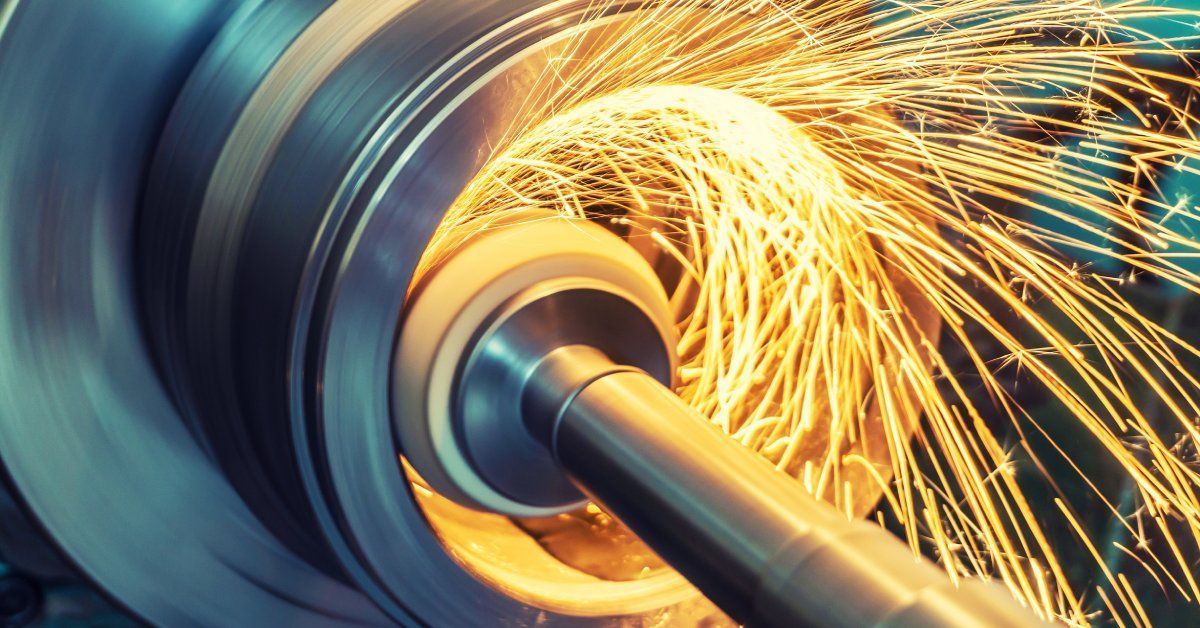 A machine in the process of grinding down a metal part attached to a long rod with sparks flying off of it.