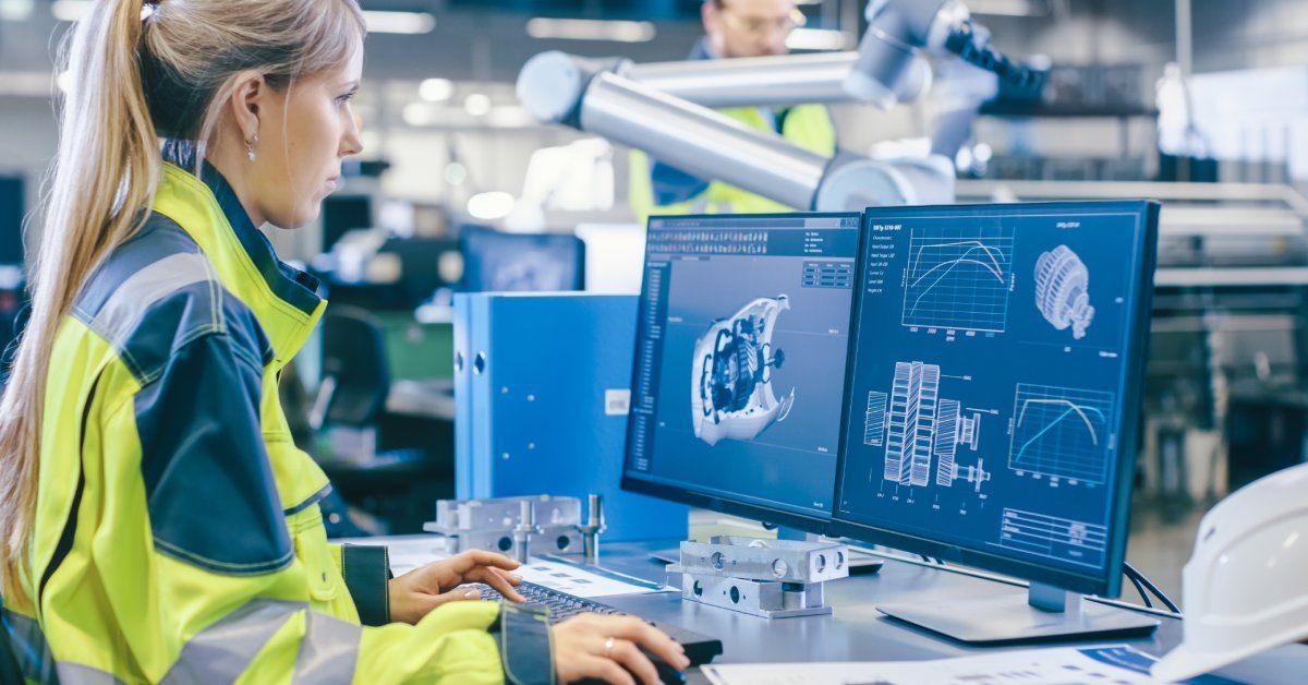 A worker wearing high-visibility clothing sitting at a desk, using a computer to design products.