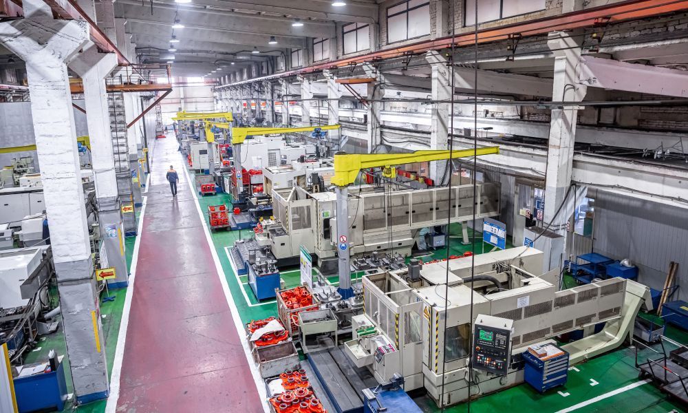 An employee walks through a brightly lit, large-scale CNC machine shop on the way to their station.