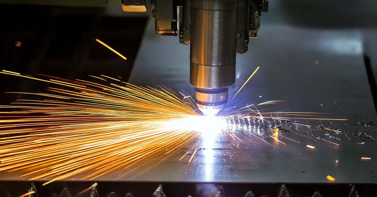 A close-up of a CNC machining laser cutting tool removing material from a piece of sheet metal, producing bright sparks.