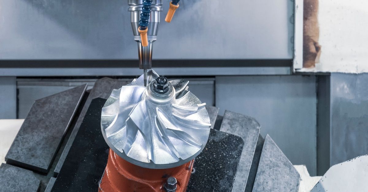 A CNC milling machine removes material with a cutting tool to produce a circular metal piece with fins as it is angled.