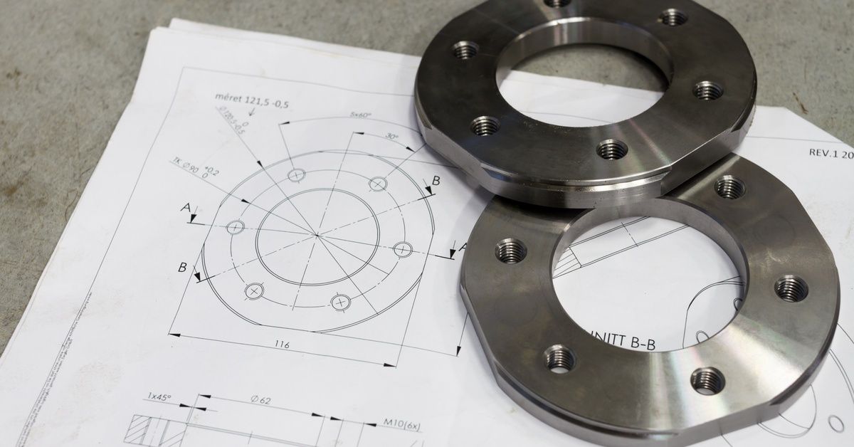 Printed design plans for a circular CNC-machined component. Two pieces of the designed part made fro