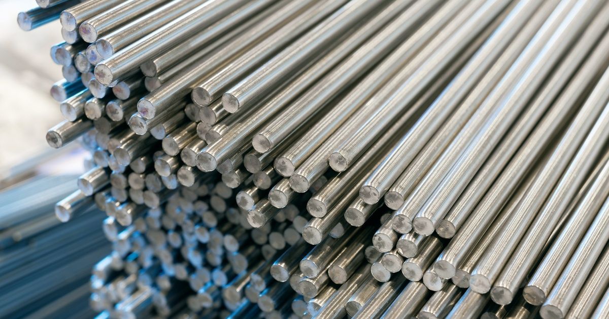 A large bundle of hundreds of thin, cylindrical stainless steel bars, up close, in a manufacturing warehouse.