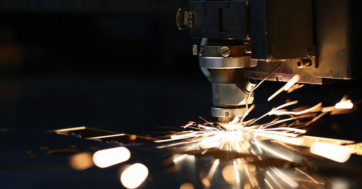 A close-up of a laser cutting tool creating bright sparks and removing material from steel.
