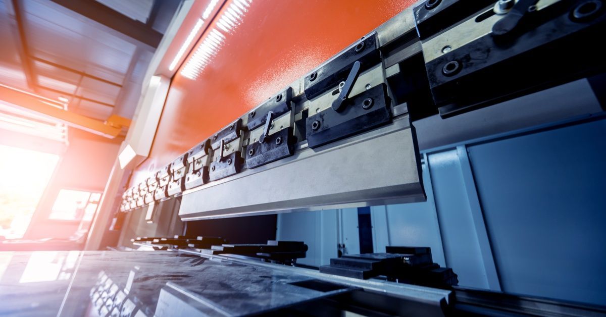 A low-angle view of a shearing machine in a metal shop. A tool to bend sheet metal is secured to the top edge of the machine.