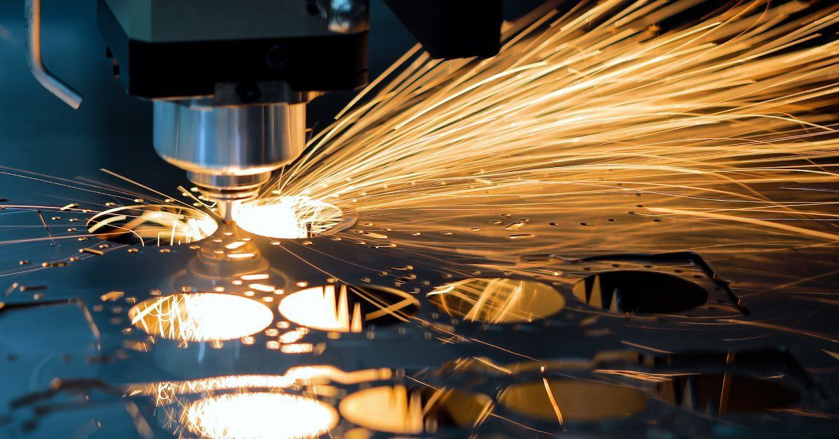 A close-up of a CNC laser cutting machine removing circular material from a flat piece of metal, creating sparks.
