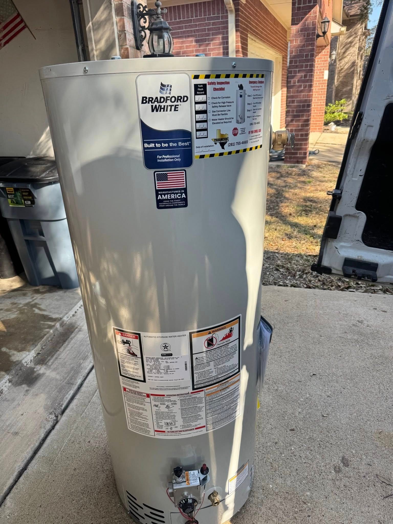 Beige water heater beside a house with warning labels and valves visible in a driveway or garage area